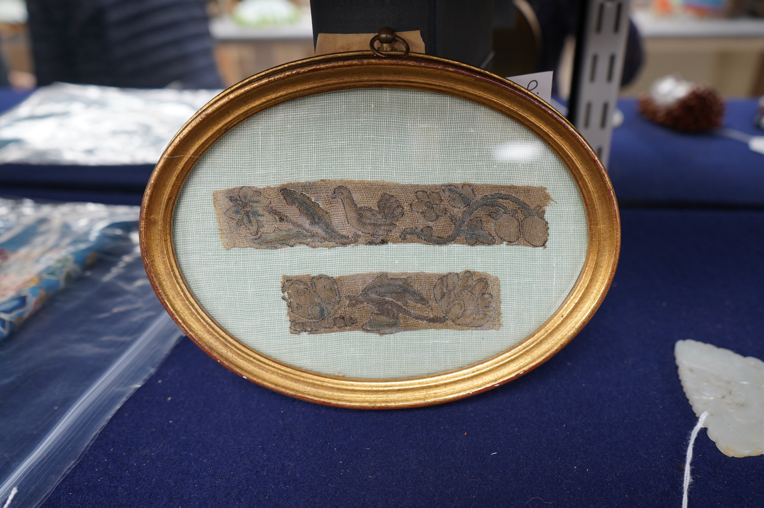 Two 17th century finely embroidered needlework fragments, possibly originally part of a casket or sampler, depicting a butterfly and flower on one and a bird and fruit on the other, in an oval gilt frame, largest fragmen